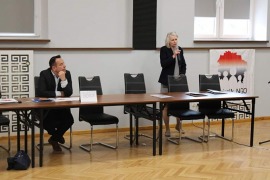 przedstawiciele Departamentu Spraw Społecznych i Zdrowia - Piotr Niedziałkowski - siedzi przodem na krześle za stołem oraz Elżbieta Wierszyło - stoi przodem za stołem z mikrofonem w ręku